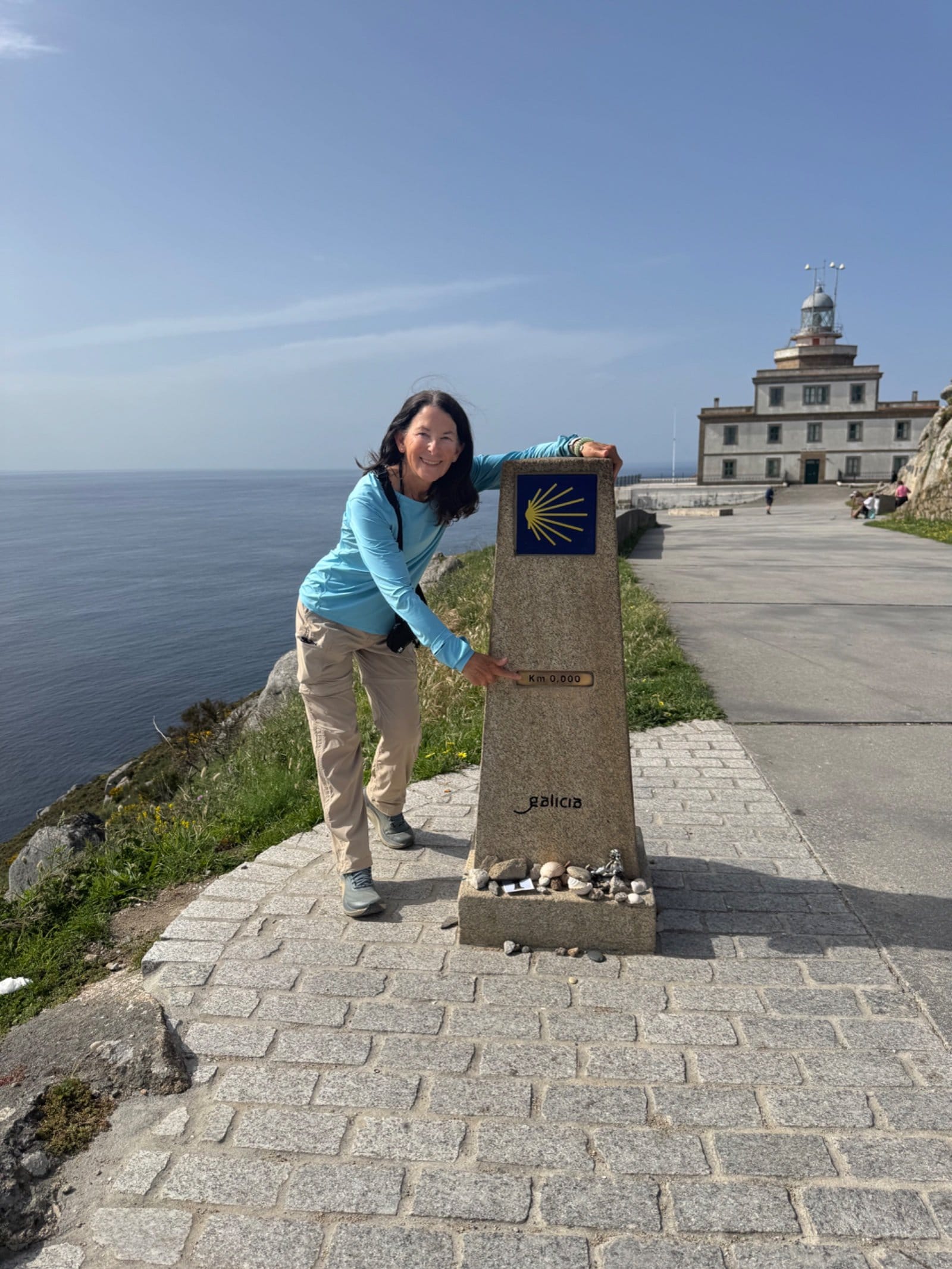 Shelley with arms around Finisterre distance marker